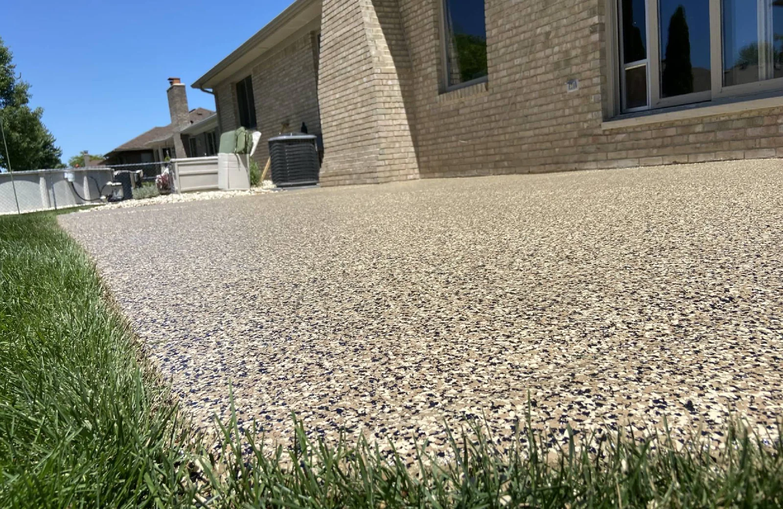 Tan flake coating on a backyard concrete patio beside a brick house