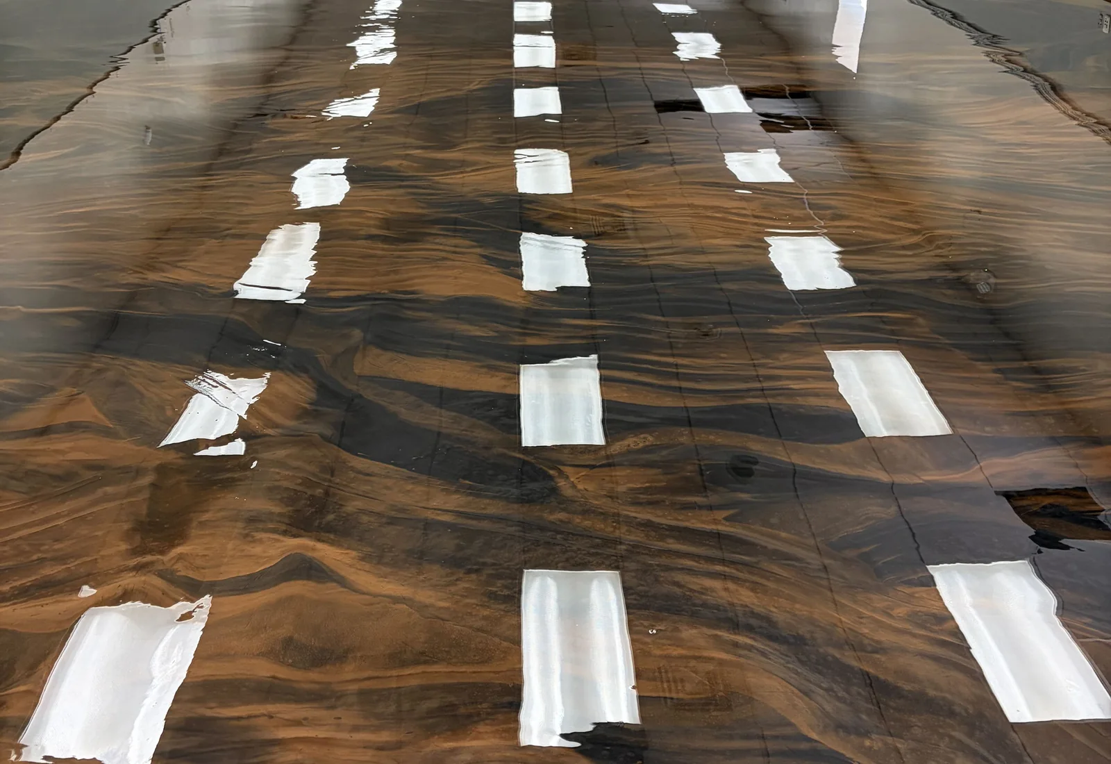 Coffee and black metallic epoxy floor by SF Huling down a long commercial room, the ceiling lights reflected in the gloss
