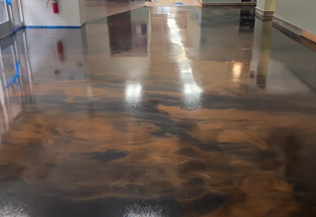 Coffee and black metallic epoxy floor beside the glass entry doors of a commercial room, painter's tape still along the wall base