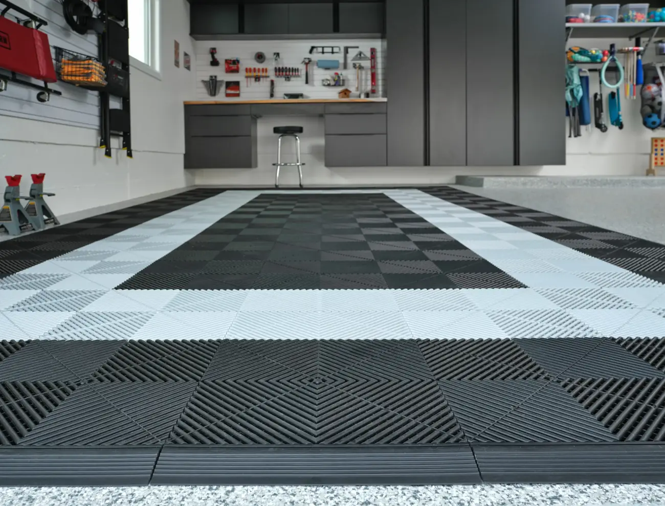 Interlocking plastic tiles laid as a parking pad on a speckled garage floor, one of the options compared with an epoxy coating