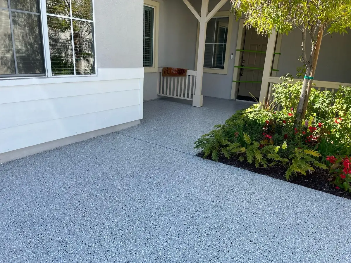 Gray flake coating on a concrete patio and front walkway beside a planting bed