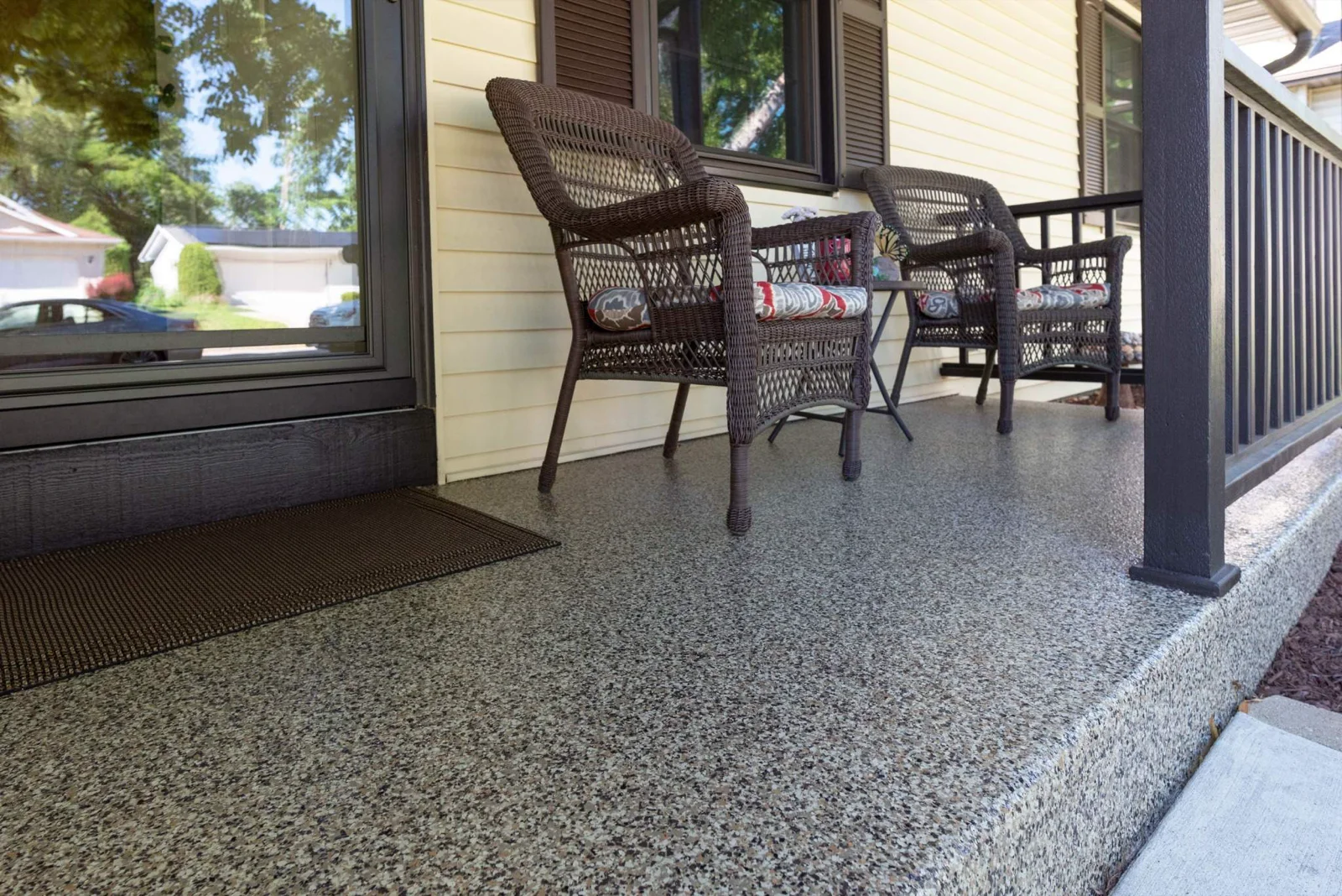 Covered front porch floor with gray and tan flake coating and wicker chairs